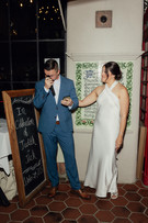 Groom becoming emotional while speaking into microphone during wedding reception speeches at State and Fig Santa Barbara while bride holds him with celebration chalkboard sign behind them