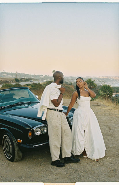 Bride and groom standing side by side beside a vintage convertible in the Malibu hills