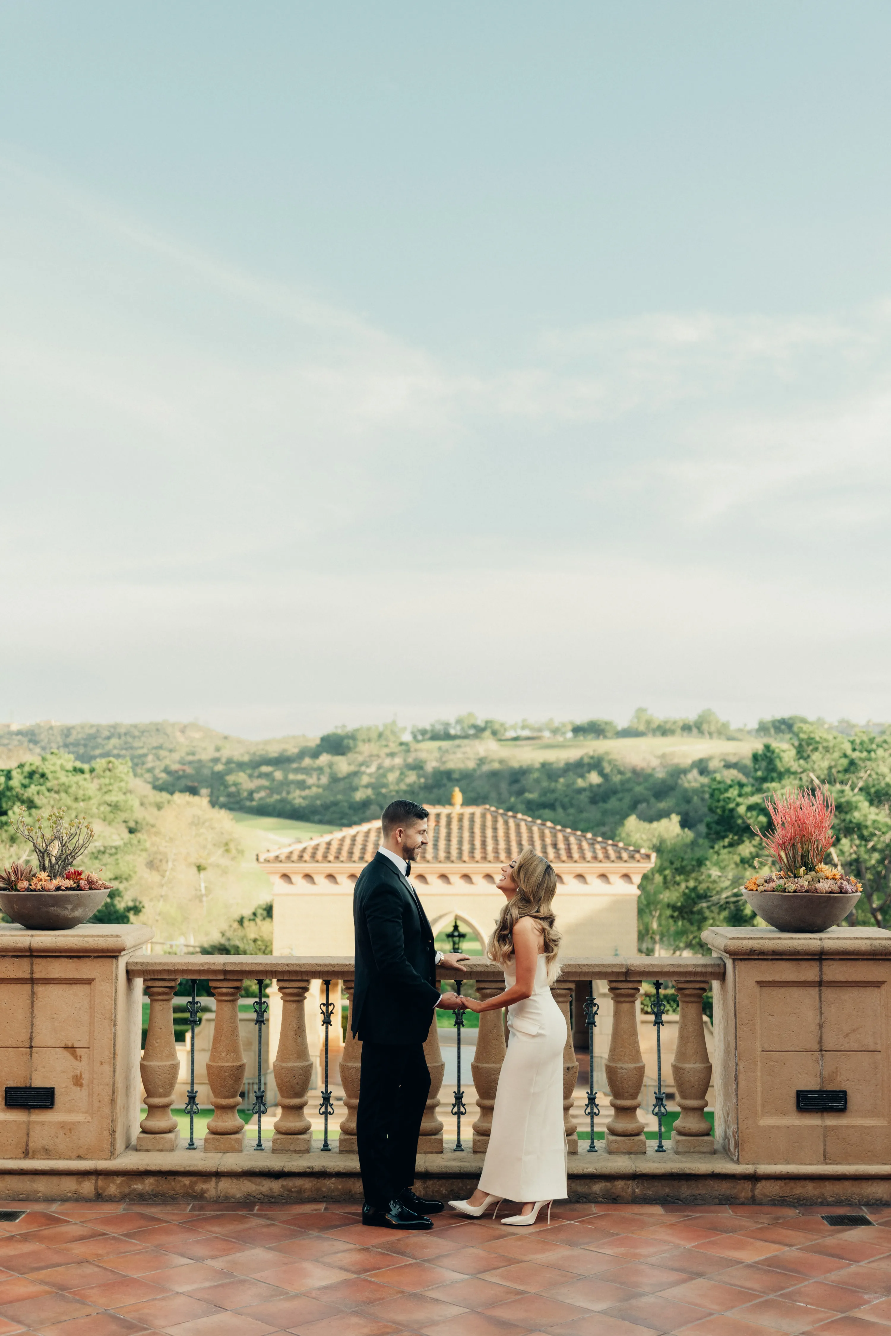 engagement photo outfits at Fairmont Grand Del Mar, couple in black suit and white gown on terrace overlooking the grounds