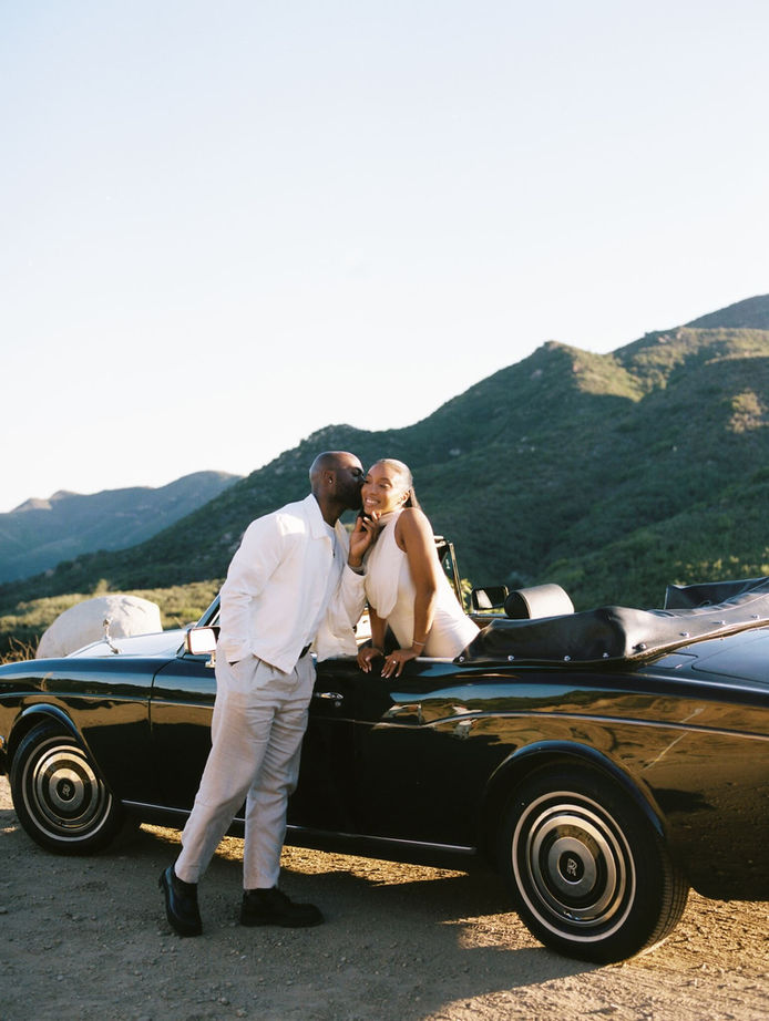 Bride and groom leaning against a vintage convertible on a Malibu hillside