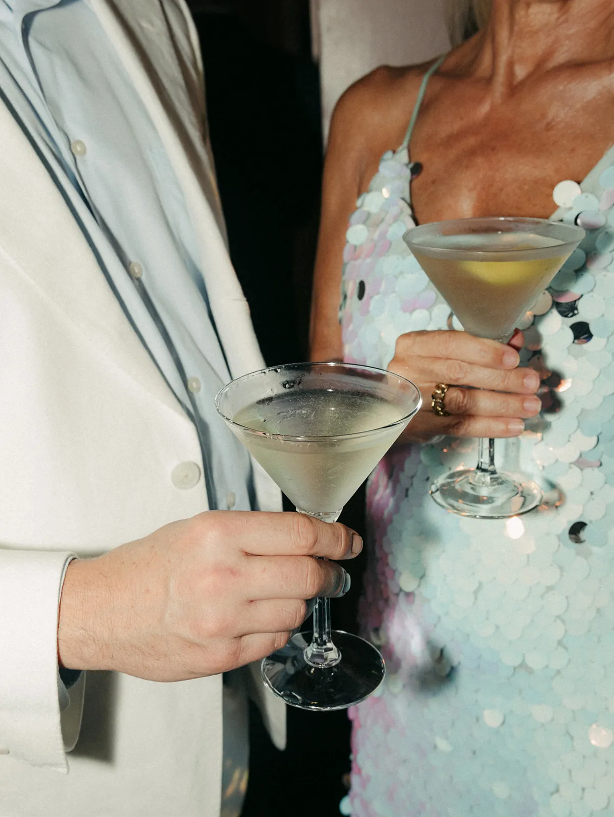 Groom in white tuxedo blazer and a sequined guest toasting martini glasses at the Catalina Island Casino wedding cocktail hour