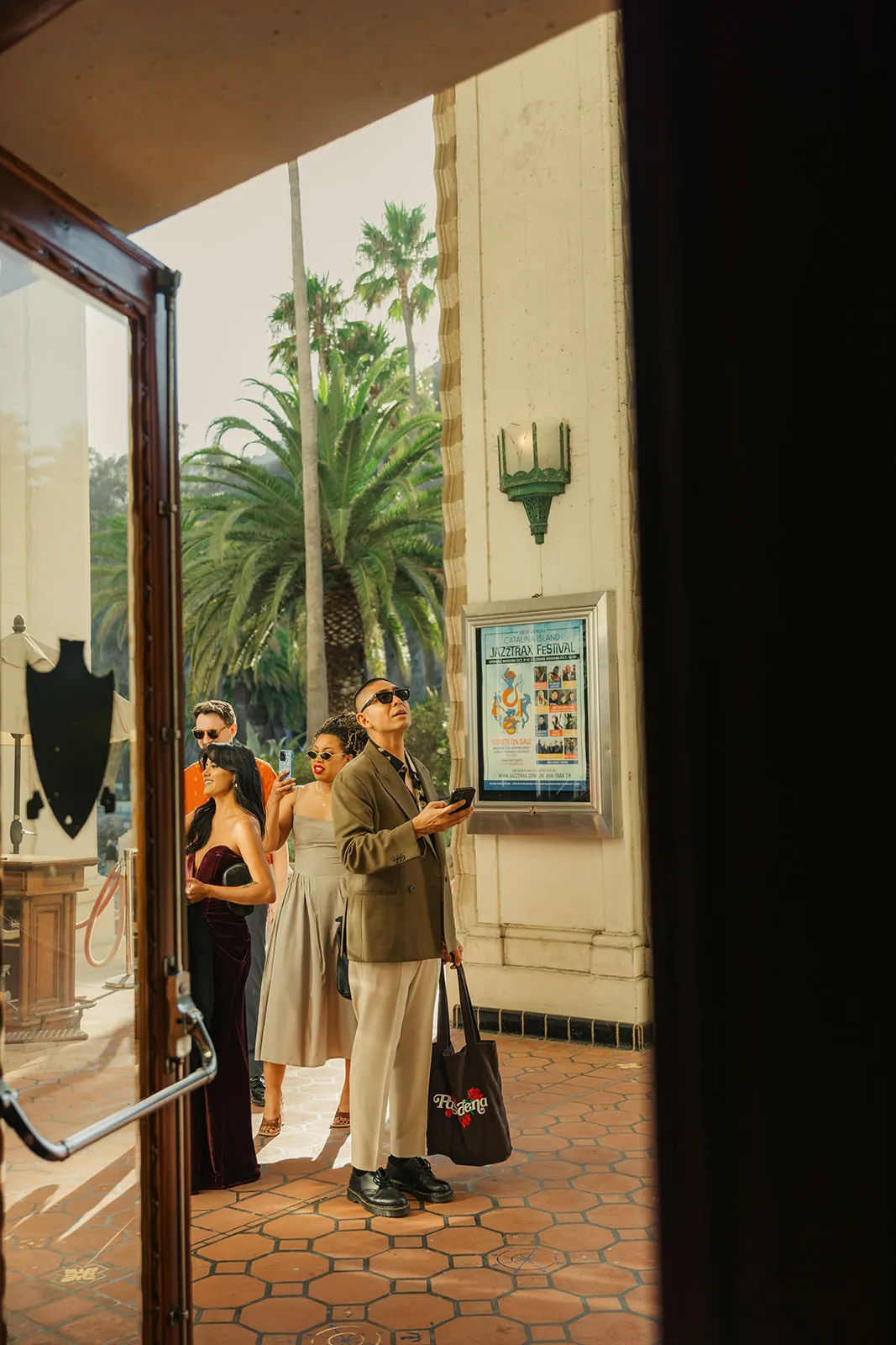 Guests looking up at the Catalina Island Casino exterior as they arrive for the wedding ceremony, Jazztrax festival poster visible on the building