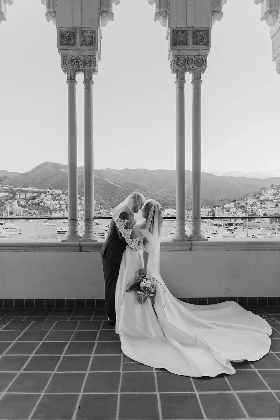 Couple sharing a dip kiss in the Casino colonnade, white columns and Avalon Bay visible, black and white — a destination wedding 26 miles from Los Angeles