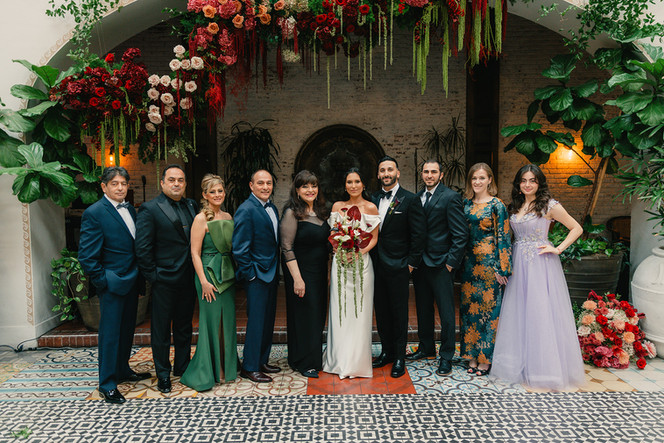 Full wedding party portrait beneath the red and green floral arch at the Ebell of Long Beach