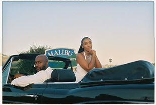 Close-up of engaged couple sitting in a vintage convertible with the Malibu sign behind them