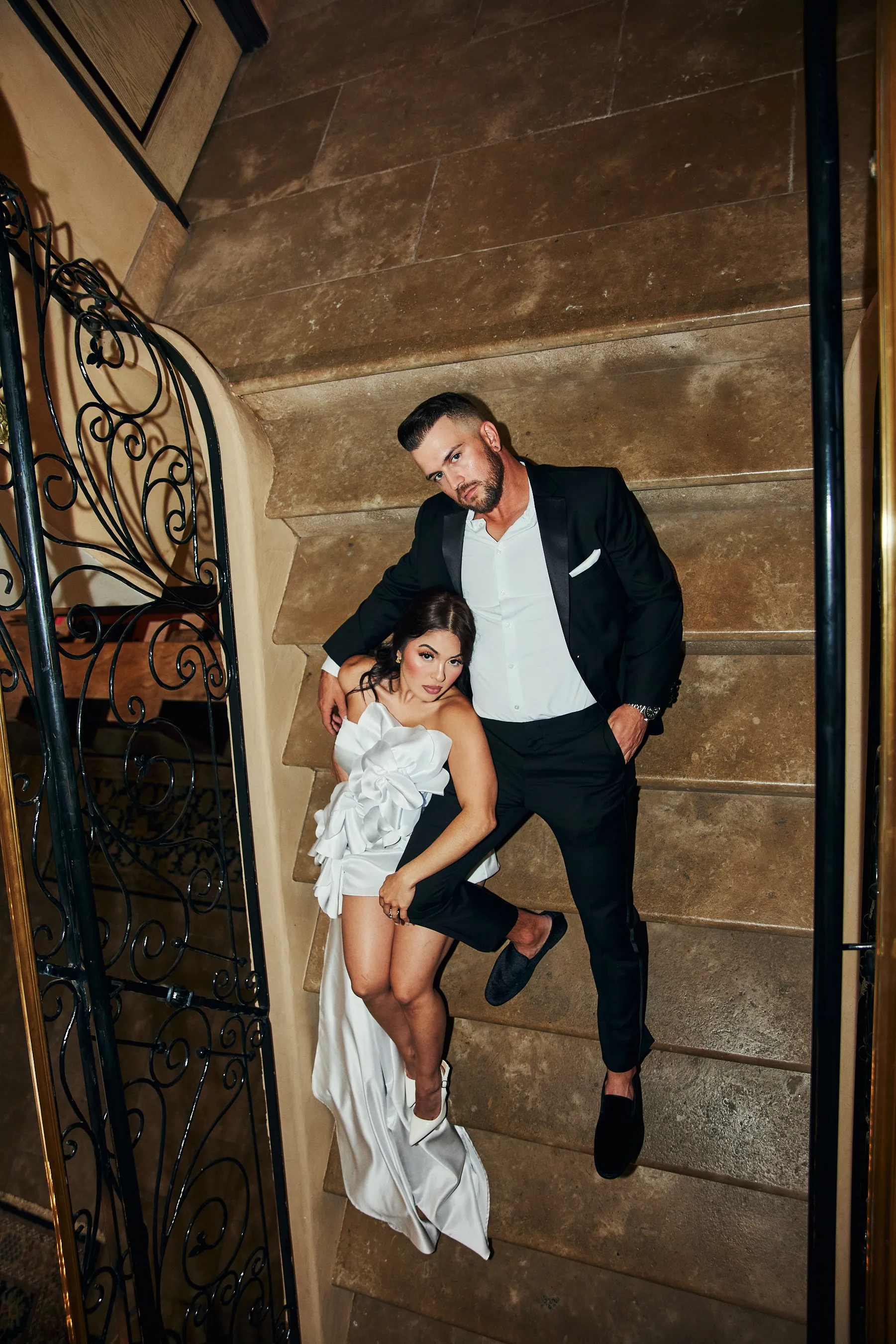 engagement photo outfits at a hotel in Los Angeles, couple in black suit and white ruffled dress on an ornate staircase