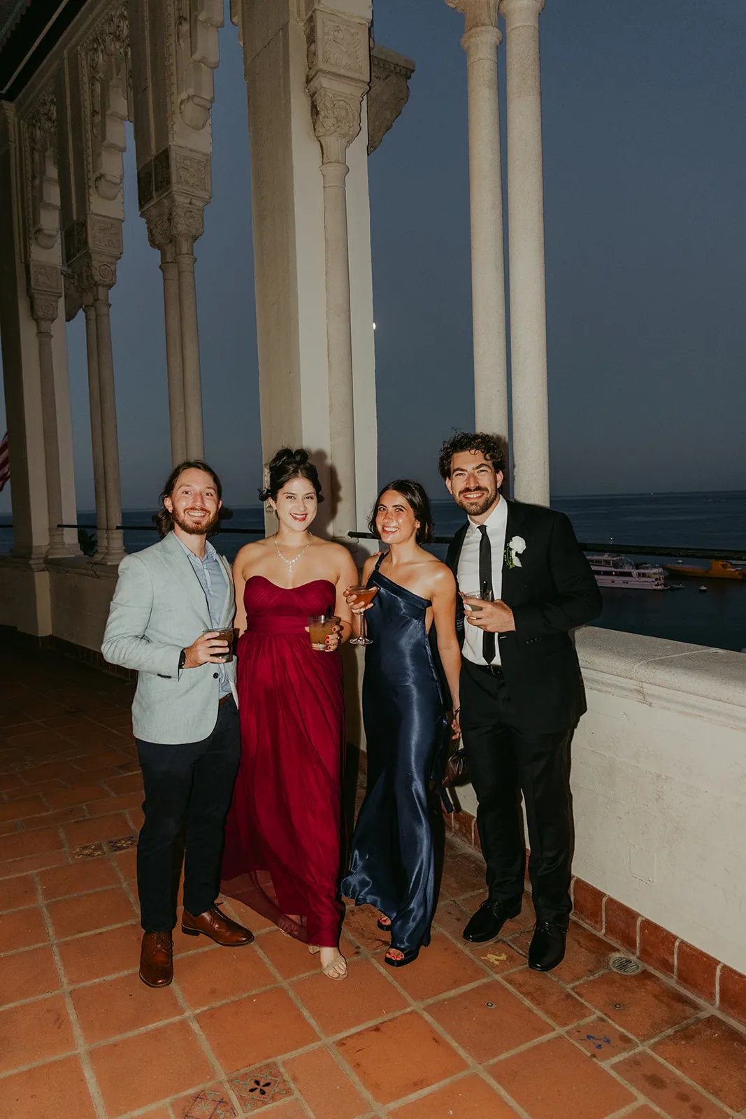 Wedding guests on the Catalina Island Casino colonnade veranda at night with cocktails, white ornate columns and harbor lights behind them