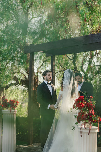 Couple exchanging vows beneath wooden arbor framed by lush greenery