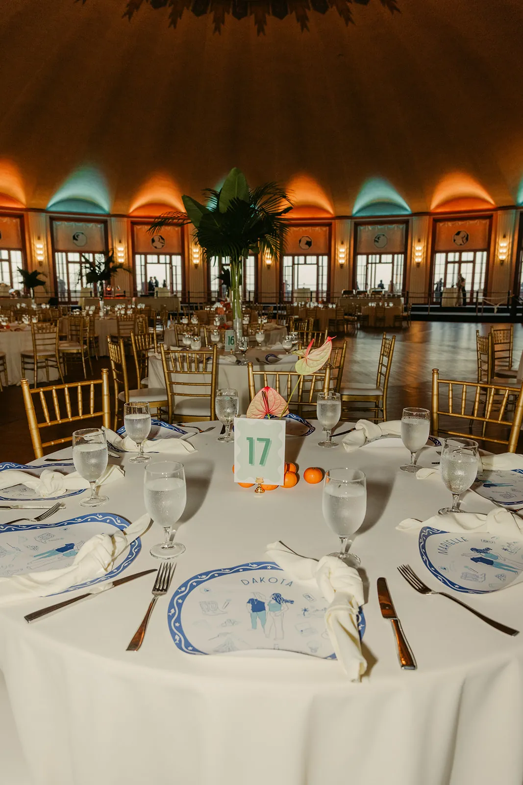 Casino Ballroom tablescape at a Catalina Island Casino wedding reception — custom illustrated placecards, anthurium centerpiece, tangerines, and table number 17 with gold chiavari chairs