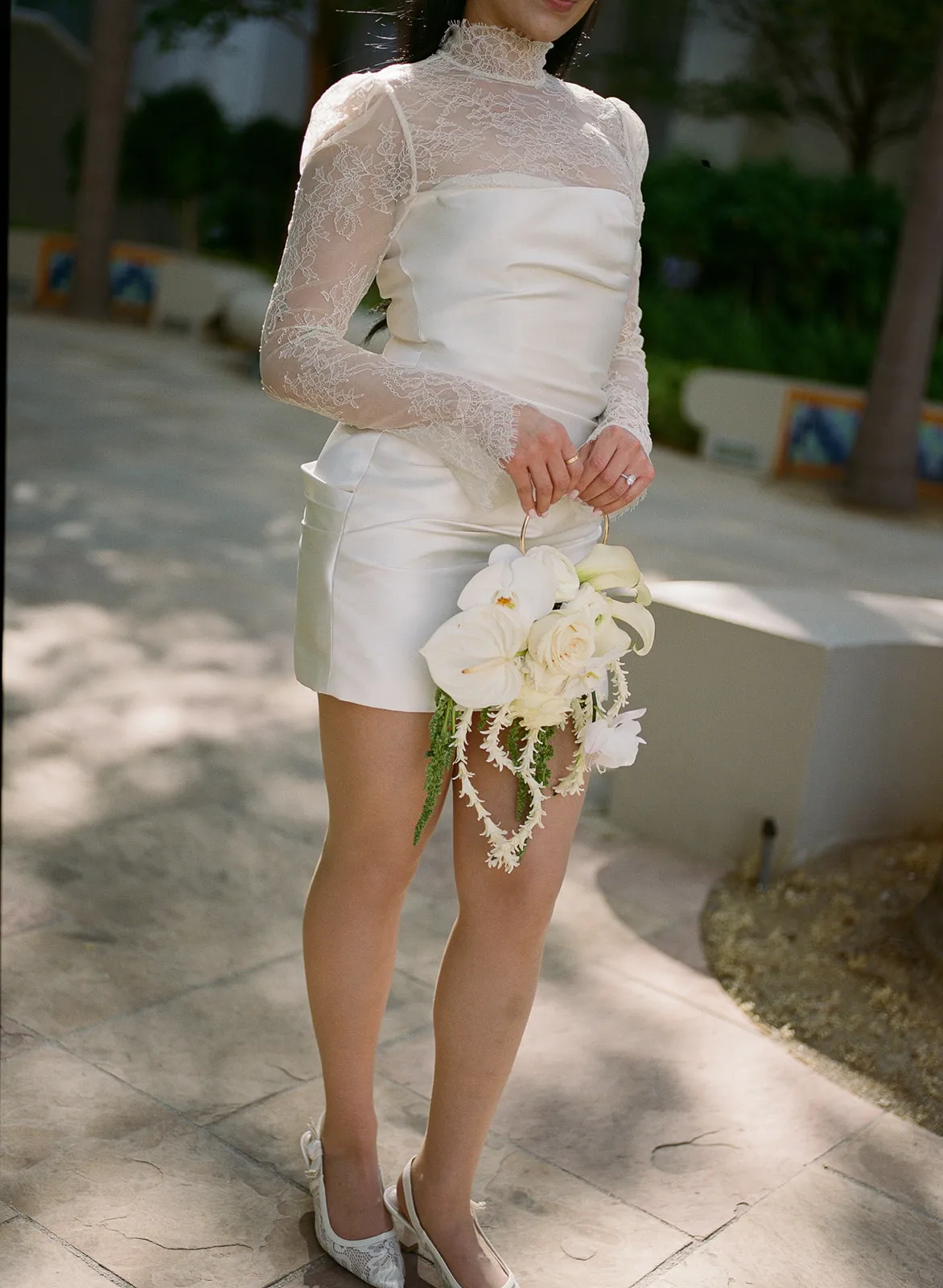 Close-up detail of bride's short white lace turtleneck wedding dress and fashion purse bouquet with white orchids, roses and trailing greenery at Beverly Hills City Hall, shot on film by Los Angeles wedding photographer Rene Porto