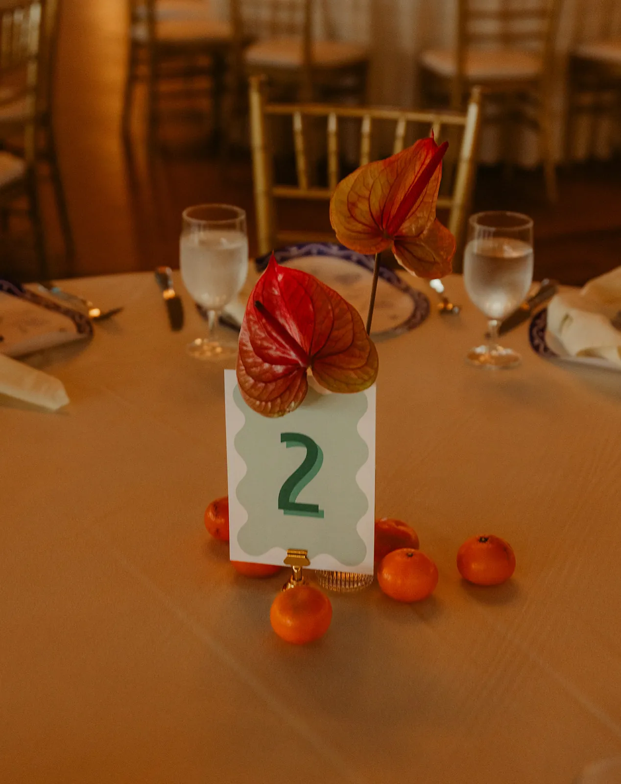 Anthurium and tropical floral centerpiece with tangerines and table number two at a Catalina Island Casino wedding reception
