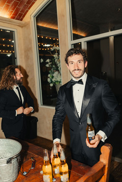 groom holding a beer while hanging out with groomsmen inside the barrel room at falkner winery in temecula