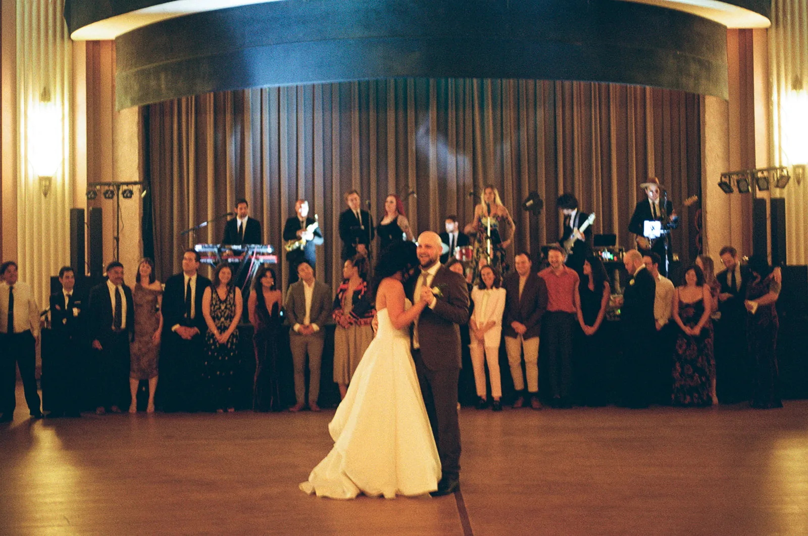 Bride and groom sharing their first dance in the Catalina Island Casino Ballroom on 35mm film, live band on stage and guests watching from the perimeter
