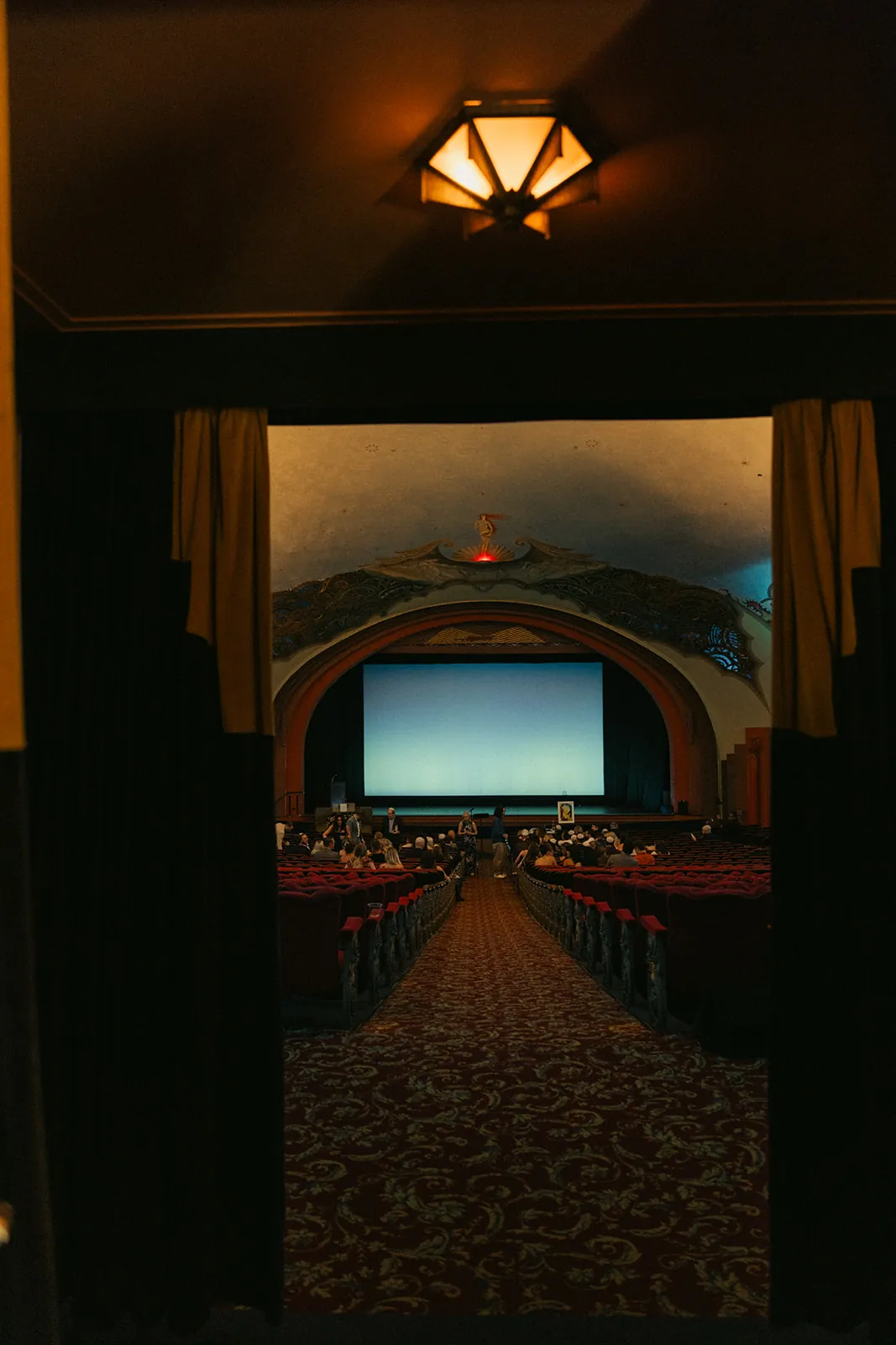 View through open doors into the Avalon Theatre at the Catalina Island Casino, red velvet seats and art deco interior visible as guests arrive for the wedding ceremony