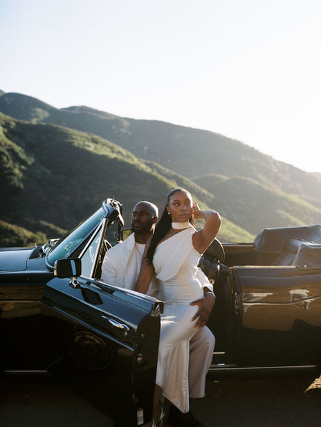Couple stepping out of a vintage convertible on a Malibu hillside overlooking the coast