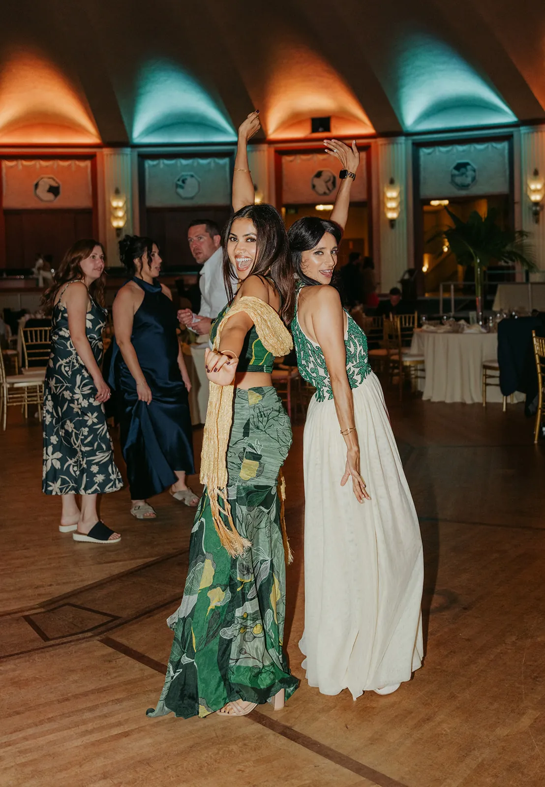 Guests dancing back to back on the Catalina Island Casino Ballroom dance floor during the wedding reception, colorful gowns and teal uplighting