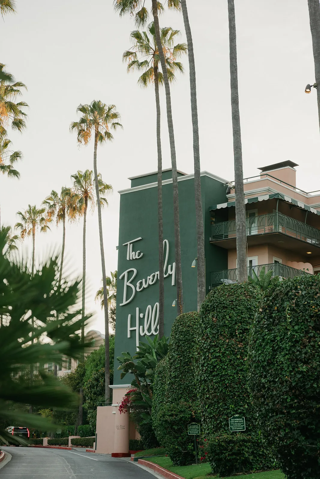 The iconic Beverly Hills Hotel green building sign surrounded by towering palm trees at dusk, a landmark location for Beverly Hills courthouse wedding photography