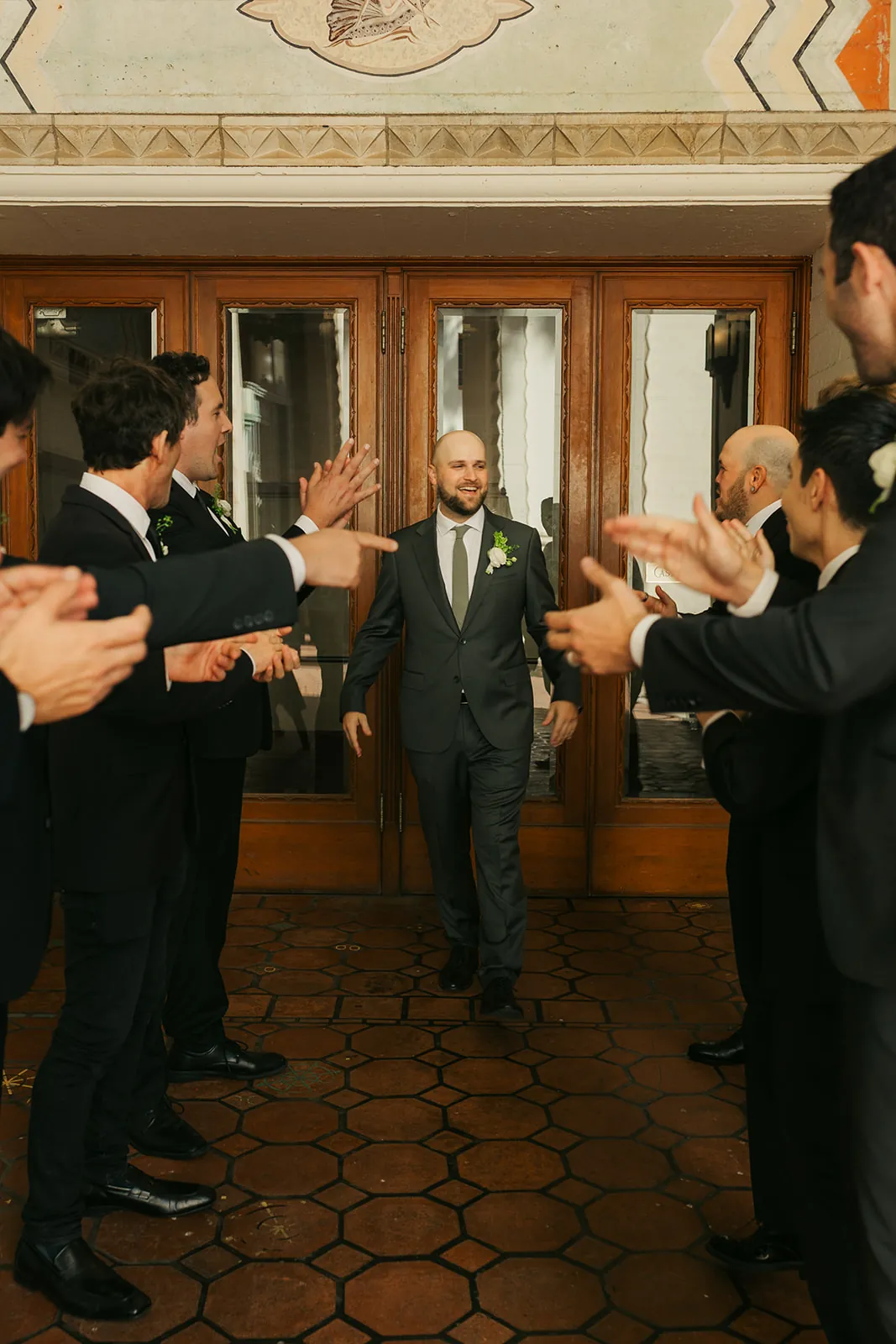 Groom walking through a groomsmen tunnel at the Catalina Island Casino entrance, art deco ceiling and mosaic tile floor visible