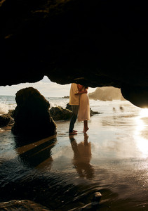 cinematic malibu beach engagement photos under sea cave with golden sunset reflections