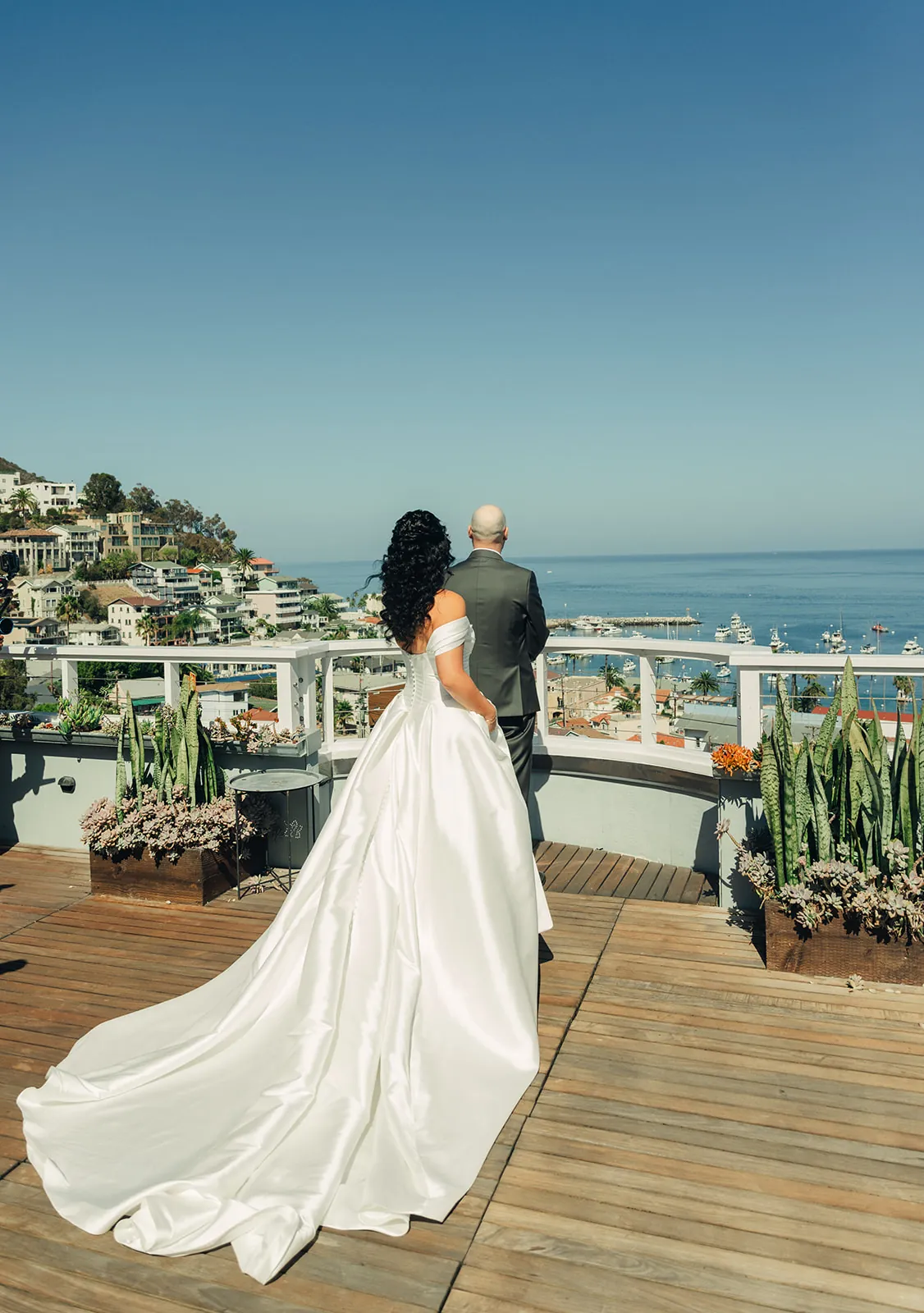 Bride and her father standing together on a rooftop with their backs to the camera, overlooking Avalon Bay at a Catalina Island Casino wedding