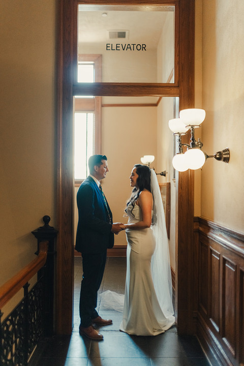 Couple standing together in the warm glow of the antique elevator hallway at the Old Orange County Courthouse elopement