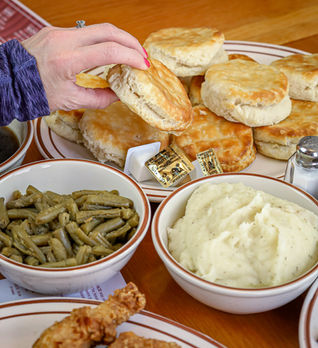Family-style Southern comfort food including fried chicken, roast beef, mashed potatoes, biscuits, green beans, and corn.