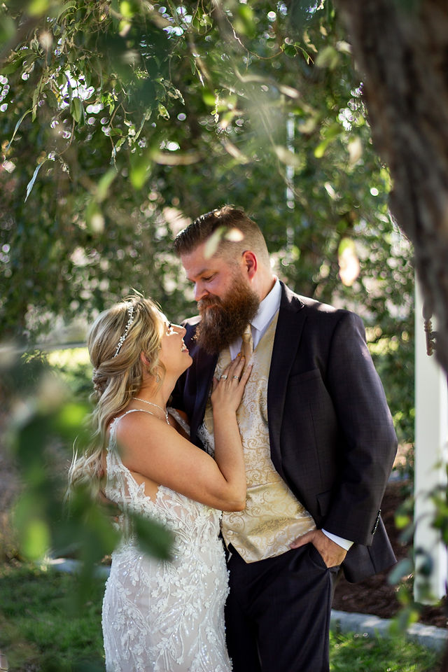 Bride and Groom standing under tree greenery looking lovingly to each other. Photo by Marie Photography
