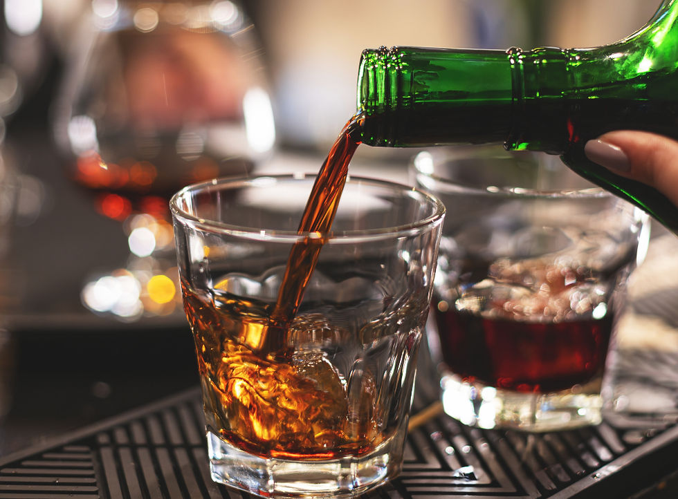A green bottle of whiskey being poured into a whiskey glass at a bar, with blurred cocktails in the background
