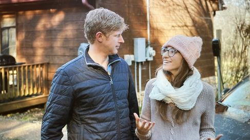 couple standing outside in front of wood home looking at each other appears to be winter environment