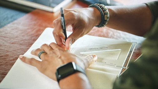man draws in notebook with angle finder