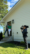 man and woman stand by side door of house with camera man in the foreground