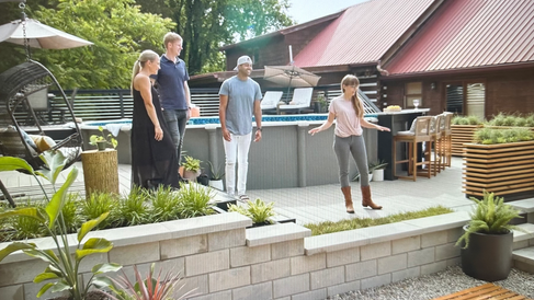 two women and men stand around pool and swinging chair on an outside deck talking to each other