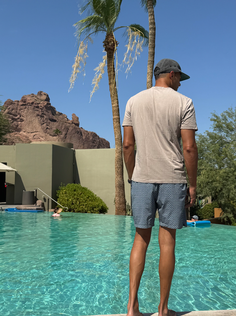 man stands at edge of pool with mountain and palm tree in the background