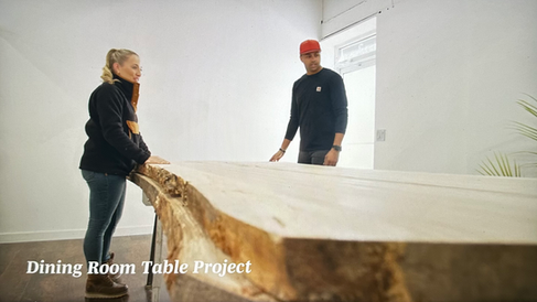Man and woman look over large wood slab in white room.