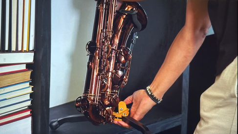 Man places copper saxophone on wooden bookshelf.