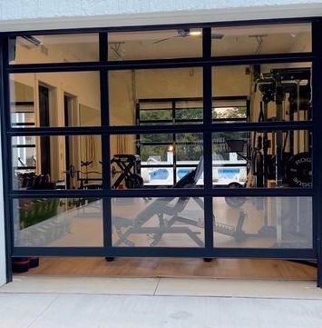Glass garage door with gym inside and various workout equipment leading to poll area on the oppositye side of home
