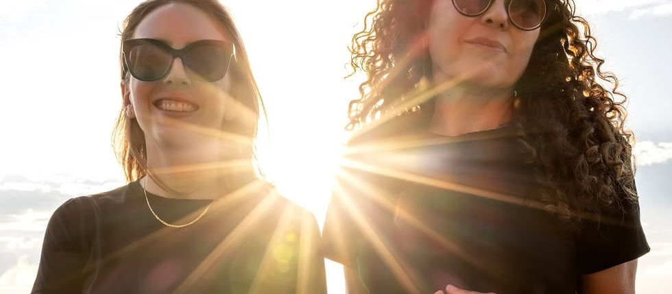 Mary Halvorson and Sylvie Courvosier wearing sunglasses with sunbeams shining from behind them