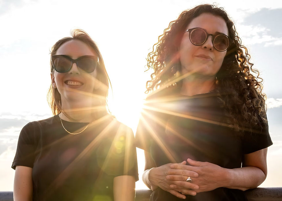 Mary Halvorson and Sylvie Courvosier wearing sunglasses with sunbeams shining from behind them