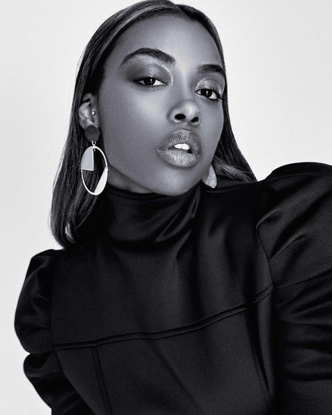 Closeup of black female model in architectural blouse, silver earring.