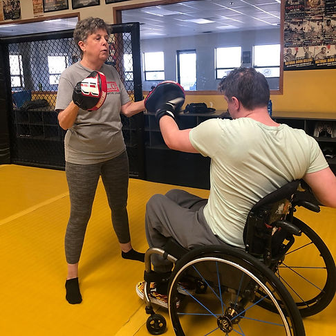 B-Bold student in wheelchair sparring with hand-held punching pads.