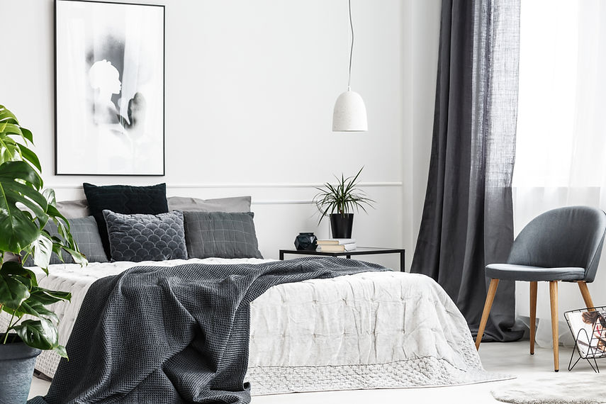 Modern, gray chair with wooden legs by a window of a bright bedroom interior with a dark g