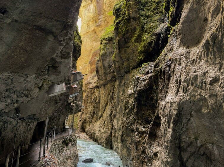 Стрімка гірська річка тече по дну вузької кам'яної ущелини Партнахкламм, зліва видно пішохідну доріжку з поручнями.