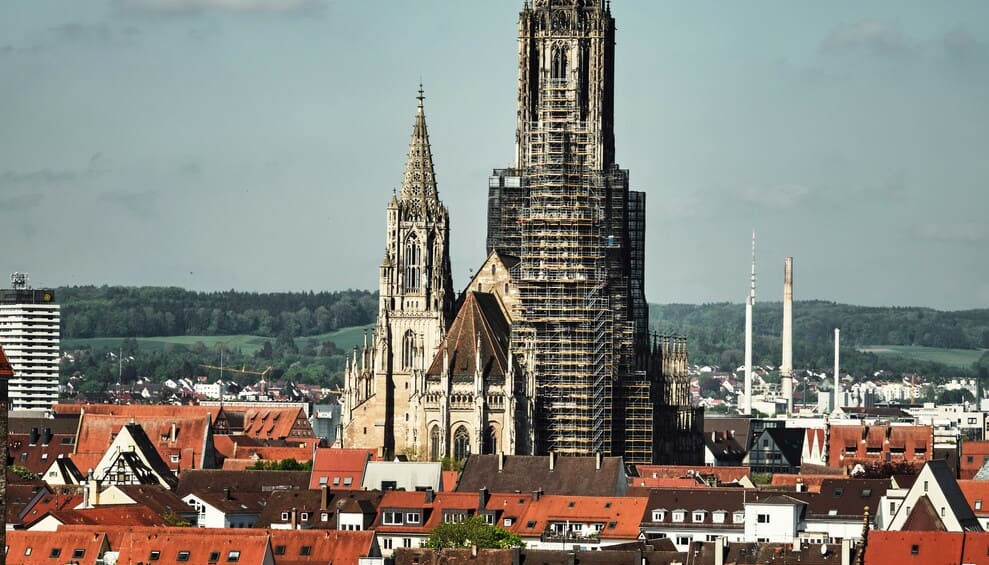 Високий темний готичний шпиль Ульмського собору, який домінує над панорамою міста з червоними дахами будинків.