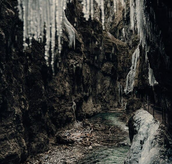 Темна кам'яна ущелина взимку, над річкою звисають гострі крижані бурульки.