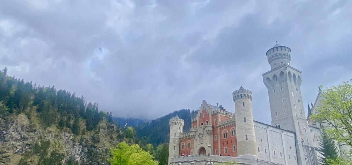 Висока кругла вежа замку Нойшванштайн з вікнами-бійницями на фоні ясного неба.