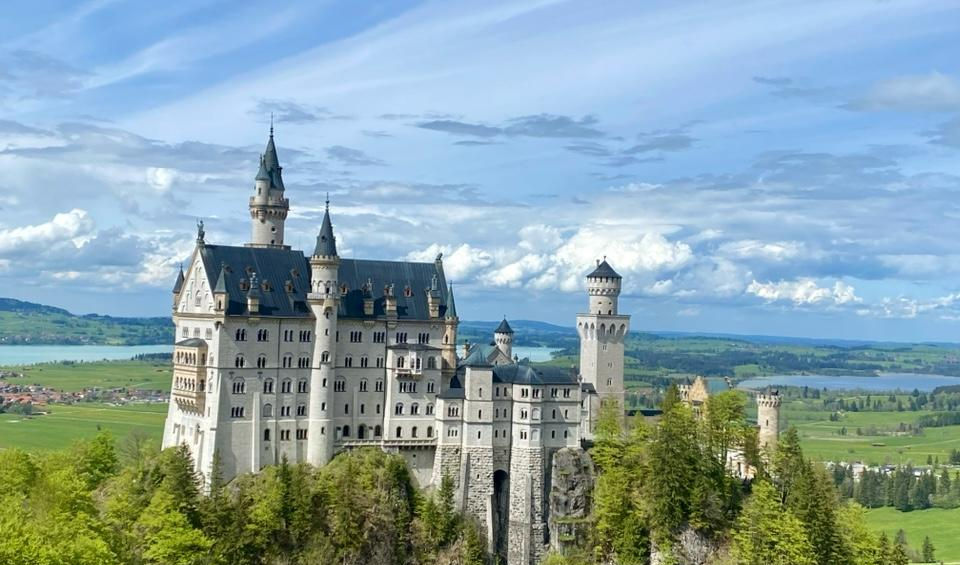 Замок Нойшванштайн на скелі, оточений яскравим осіннім лісом та горами.