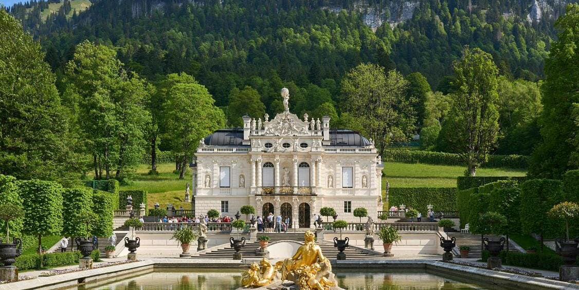 Золотий фонтан Флори в басейні перед розкішним білим фасадом баварського замку Ліндергоф.