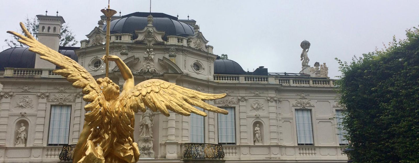 Золота скульптура ангела перед світлим фасадом баварського замку Ліндерхоф.