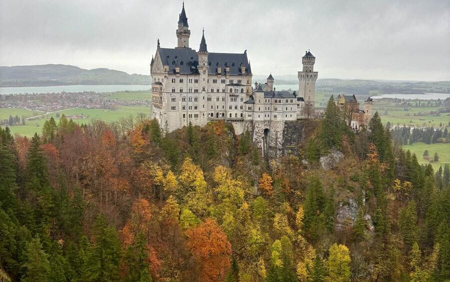 Білий замок Нойшванштайн серед яскравого жовто-червоного осіннього листя гірського лісу.
