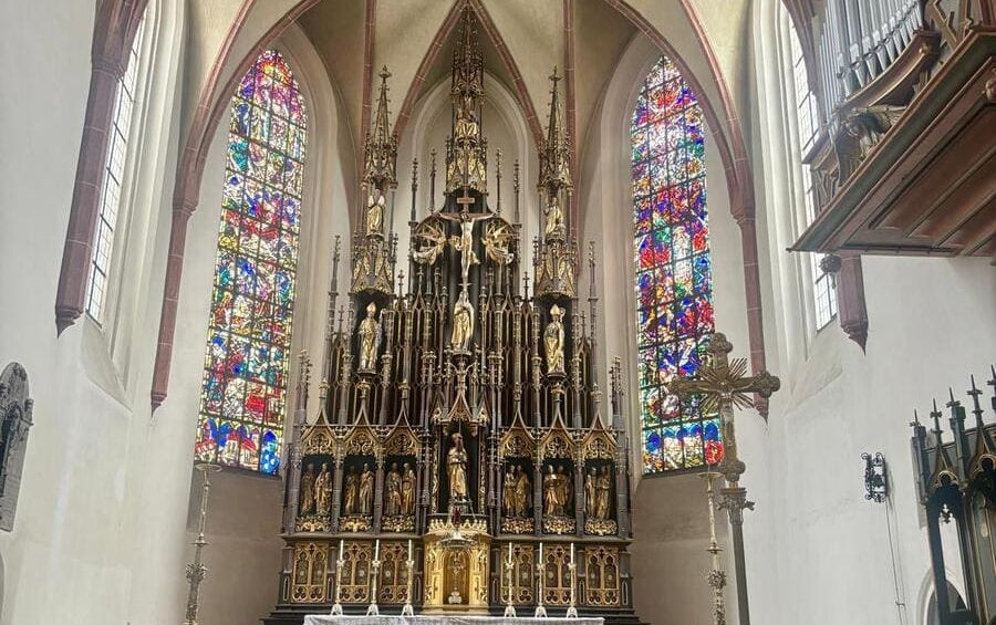 Високий дерев'яний готичний вівтар з позолоченими фігурами та кольорові вітражі в церкві.